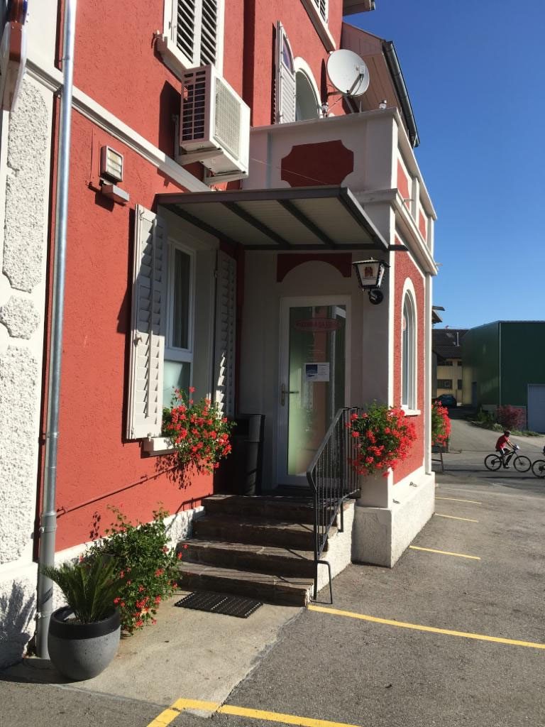 Der Eingang mit Treppe und Vordach, rote Fassade mit weissen Faschen