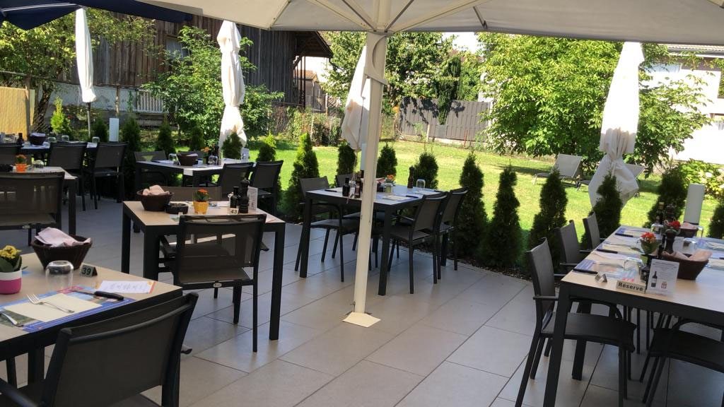 Der Garten mit Sonnenschirmen, Stühlen und einer Hecke im Hintergrund