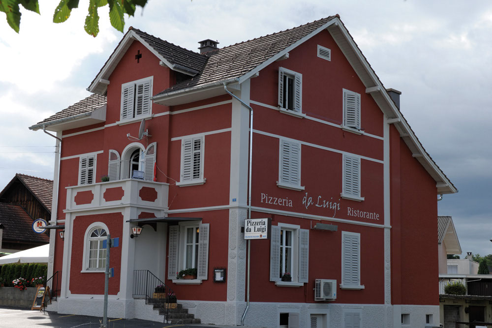 Das Haus der Pizzeria da Luigi: ein freistehendes Gebäude mit rotem Verputz, weissen Fensterläden und dem Schriftzug Pizzeria da Luigi Ristorante an der Fassade
