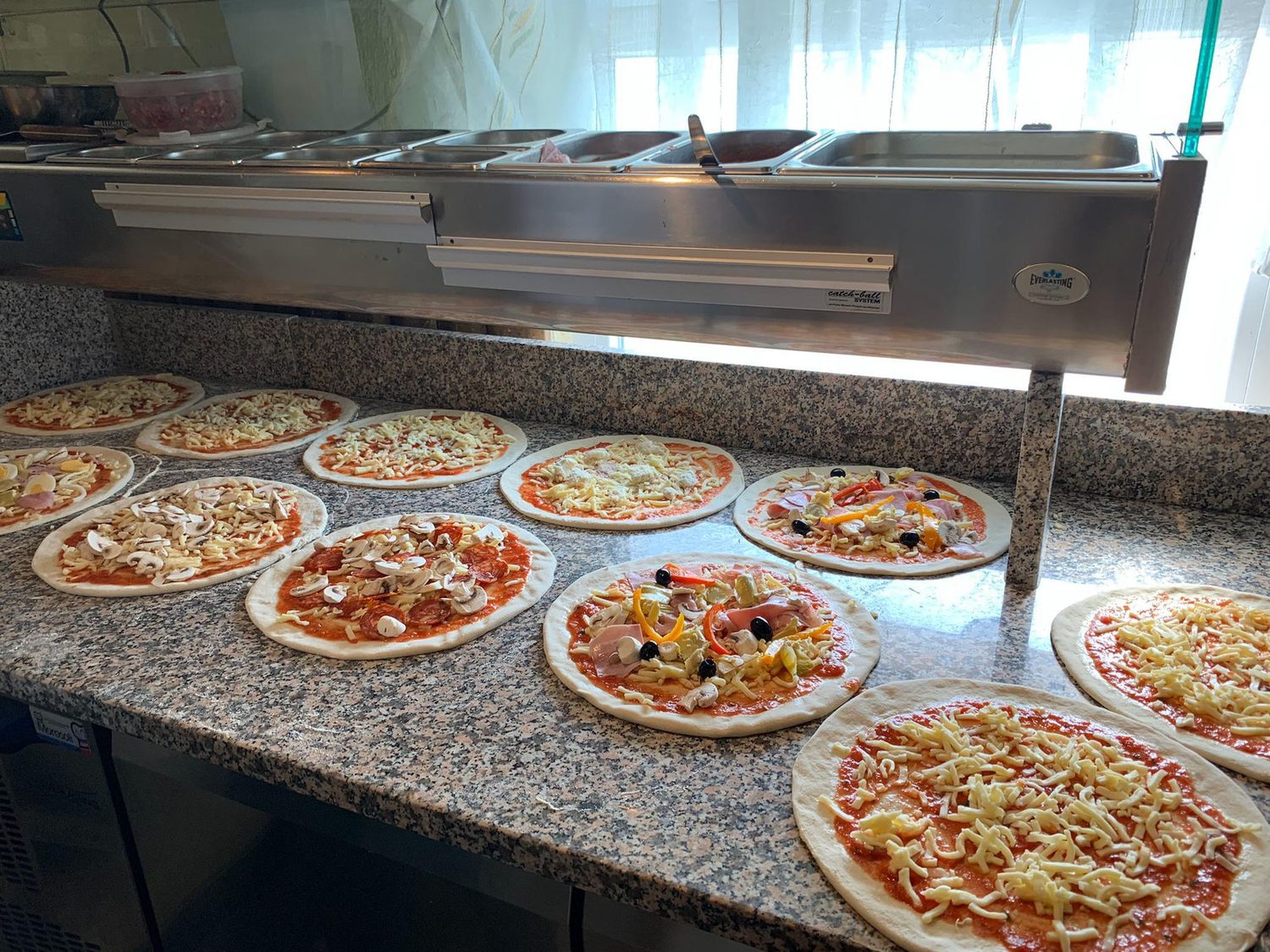 Ein Dutzend frisch belegte Pizzen auf dem Arbeitstisch, bereit für den Ofen